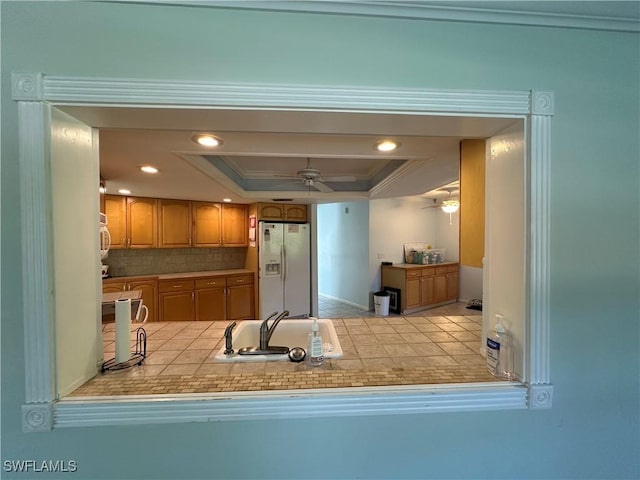 kitchen featuring sink, crown molding, white fridge with ice dispenser, decorative backsplash, and a raised ceiling