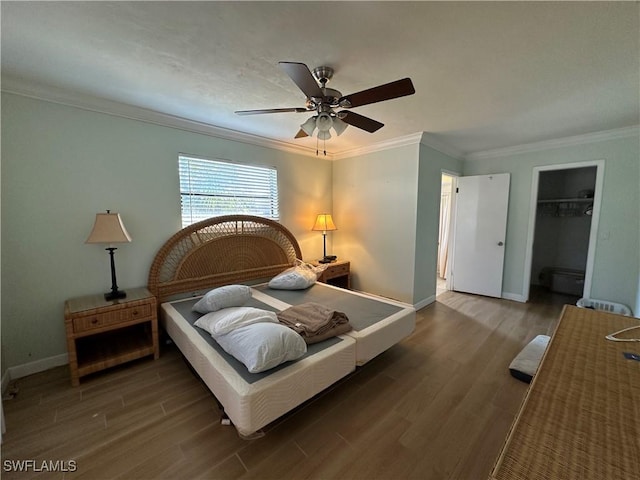 bedroom with wood-type flooring, ornamental molding, a walk in closet, ceiling fan, and a closet