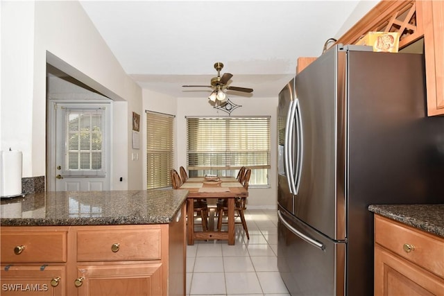 kitchen with ceiling fan, stainless steel refrigerator, dark stone counters, and light tile patterned flooring