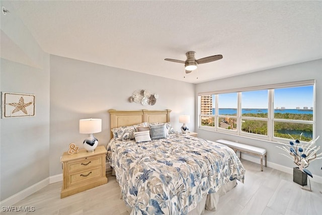 bedroom with light hardwood / wood-style flooring, ceiling fan, and a water view