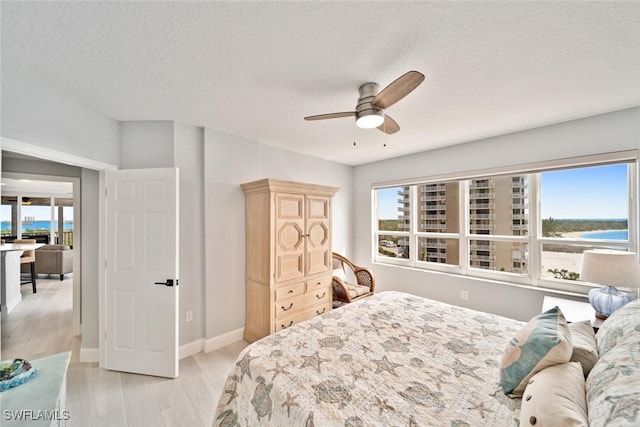 bedroom with ceiling fan, light wood-type flooring, a textured ceiling, and a water view