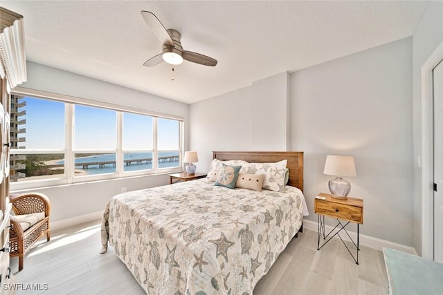 bedroom with a water view, ceiling fan, and light hardwood / wood-style flooring