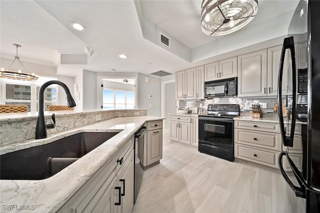 kitchen with pendant lighting, sink, backsplash, light stone counters, and black appliances