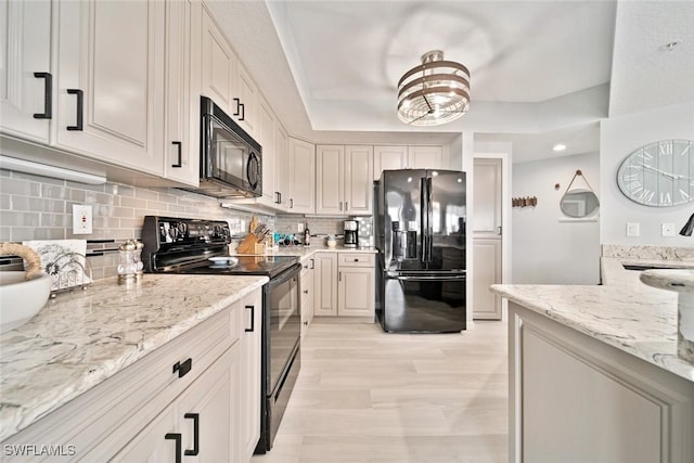 kitchen featuring light stone counters, tasteful backsplash, black appliances, and white cabinets