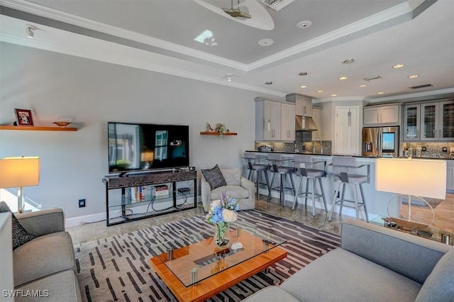 living room with a tray ceiling, recessed lighting, baseboards, and ornamental molding