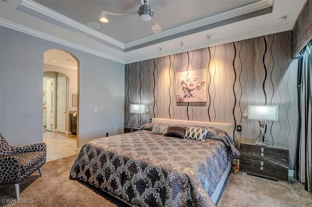 carpeted bedroom featuring arched walkways, ceiling fan, a tray ceiling, and ornamental molding