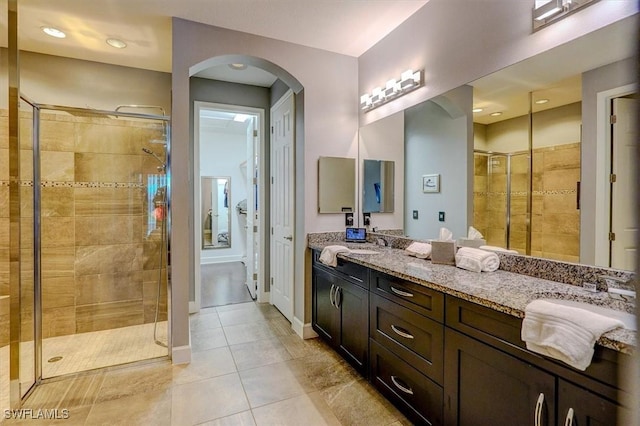 bathroom featuring a shower stall, double vanity, baseboards, and a sink