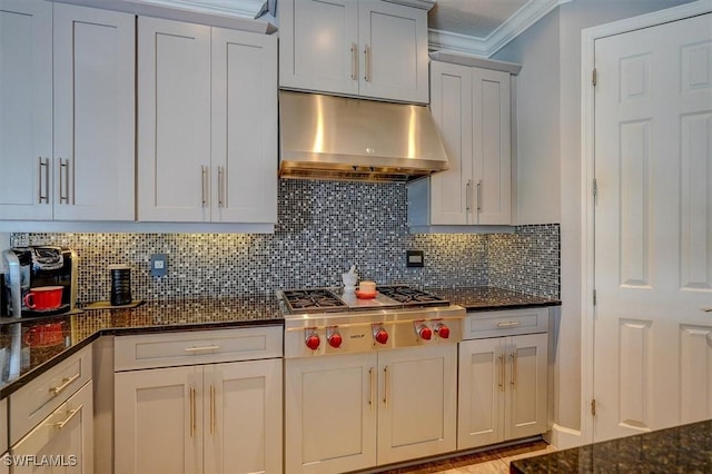 kitchen with under cabinet range hood, dark stone countertops, crown molding, decorative backsplash, and stainless steel gas cooktop