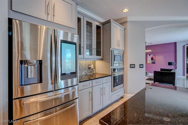 kitchen featuring dark stone countertops, stainless steel appliances, glass insert cabinets, crown molding, and backsplash