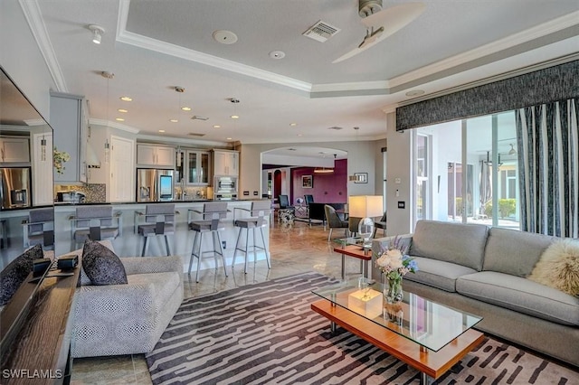 living room with a tray ceiling, crown molding, arched walkways, and visible vents