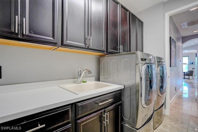 washroom with baseboards, cabinet space, arched walkways, a sink, and washer and clothes dryer