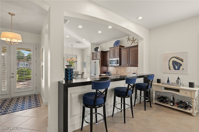 kitchen featuring appliances with stainless steel finishes, dark brown cabinets, a kitchen breakfast bar, decorative light fixtures, and kitchen peninsula