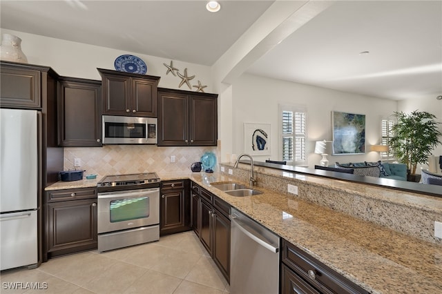 kitchen with sink, backsplash, stainless steel appliances, light stone countertops, and light tile patterned flooring