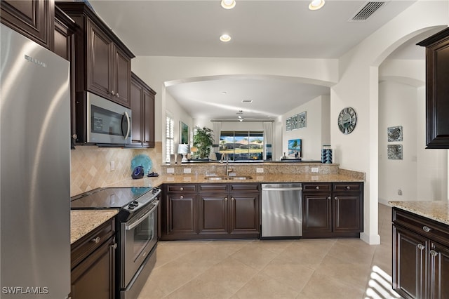 kitchen featuring sink, decorative backsplash, light stone counters, stainless steel appliances, and dark brown cabinets