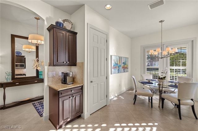 kitchen featuring tasteful backsplash, dark brown cabinets, light stone counters, and decorative light fixtures