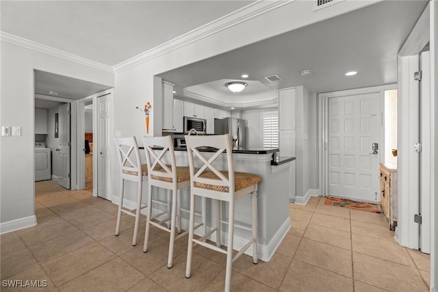 kitchen featuring appliances with stainless steel finishes, white cabinetry, a kitchen breakfast bar, washer / dryer, and kitchen peninsula