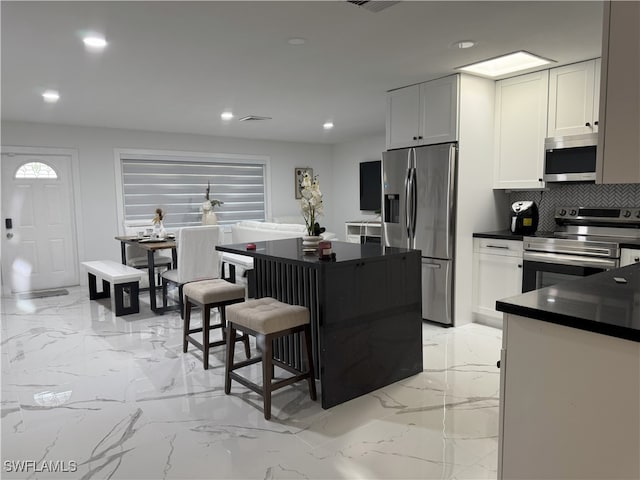 kitchen with white cabinets, stainless steel appliances, a kitchen breakfast bar, and tasteful backsplash