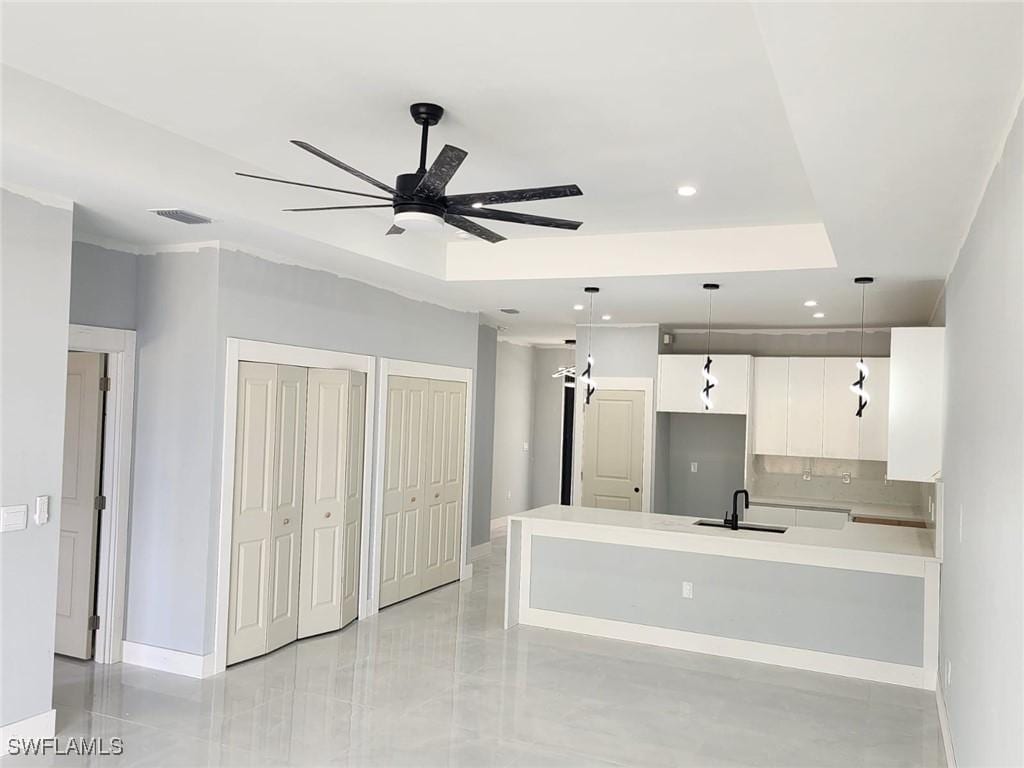 kitchen with sink, ceiling fan, hanging light fixtures, a tray ceiling, and white cabinets