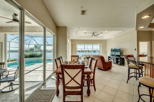 dining space with a raised ceiling, light tile patterned floors, and ceiling fan