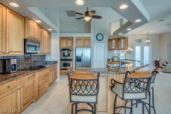 kitchen featuring stainless steel appliances, a breakfast bar area, dark stone countertops, and a kitchen island with sink