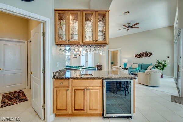 bar with light tile patterned flooring, dark stone countertops, wine cooler, and ceiling fan