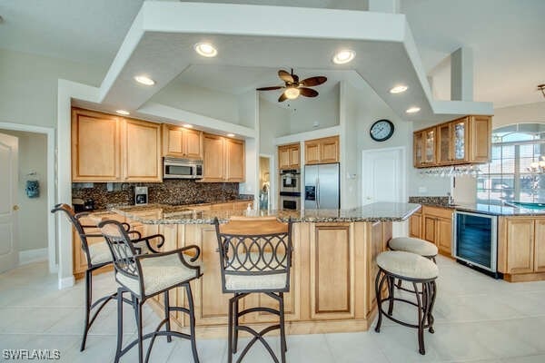 kitchen featuring a kitchen bar, tasteful backsplash, stainless steel appliances, beverage cooler, and light stone countertops