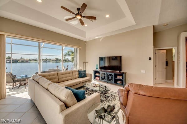 tiled living room with a water view, ceiling fan, and a tray ceiling