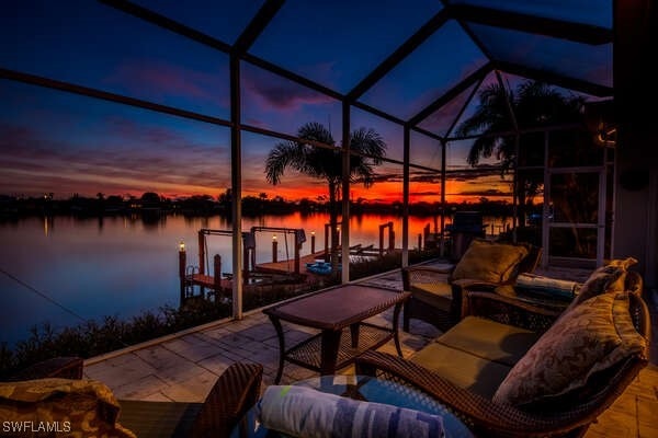 patio terrace at dusk featuring a water view, a boat dock, and glass enclosure