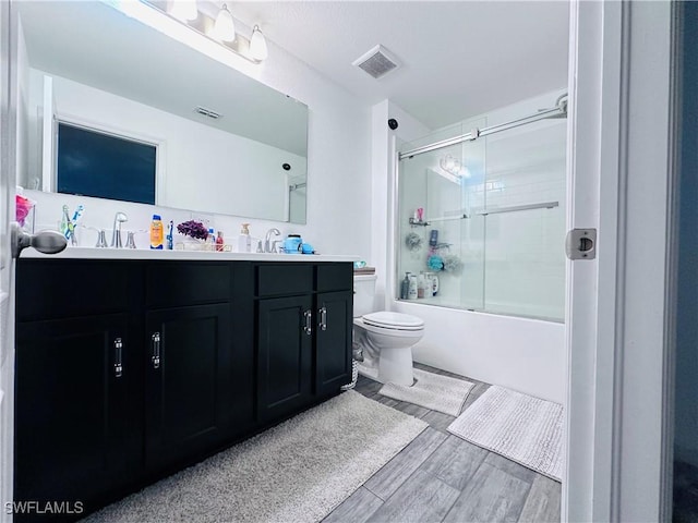 full bathroom featuring vanity, hardwood / wood-style flooring, bath / shower combo with glass door, and toilet