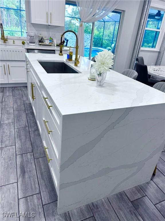 kitchen featuring light stone countertops, sink, a center island with sink, and white cabinets