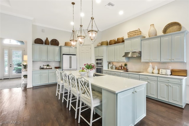 kitchen featuring high end white fridge, a breakfast bar area, hanging light fixtures, a kitchen island with sink, and black electric cooktop