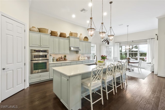 kitchen featuring sink, a kitchen breakfast bar, an island with sink, decorative light fixtures, and stainless steel double oven