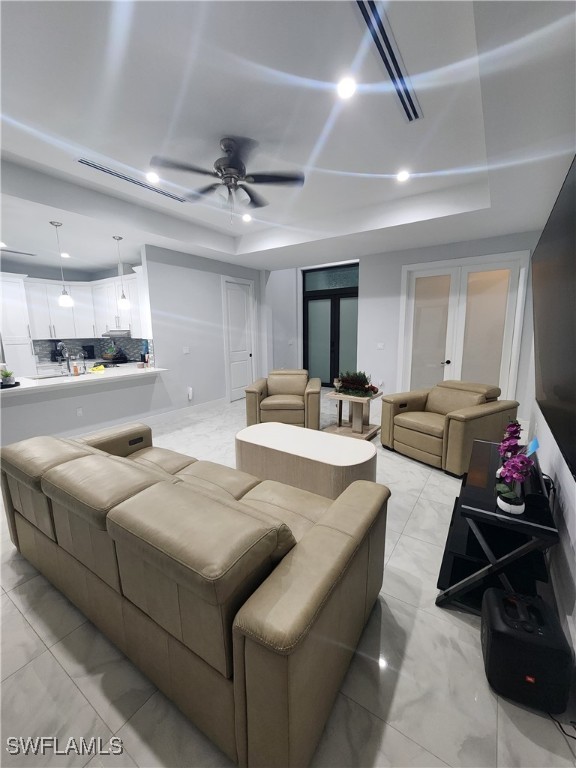 living room with a raised ceiling, ceiling fan, and french doors