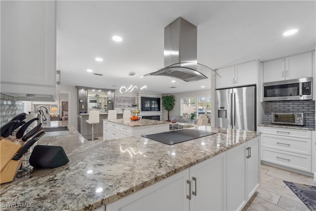 kitchen featuring light stone counters, a center island, island exhaust hood, stainless steel appliances, and white cabinetry