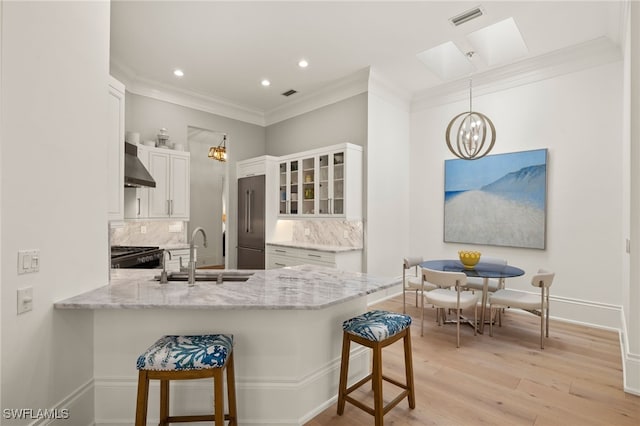 kitchen featuring wall chimney exhaust hood, high end refrigerator, hanging light fixtures, kitchen peninsula, and white cabinets