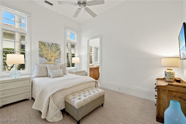 bedroom with ceiling fan, light colored carpet, and ensuite bath