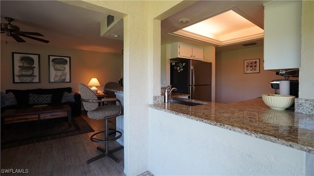 kitchen featuring light stone counters, wood finished floors, a sink, white cabinets, and freestanding refrigerator