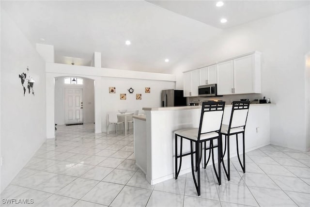 kitchen with appliances with stainless steel finishes, white cabinetry, high vaulted ceiling, a kitchen breakfast bar, and kitchen peninsula