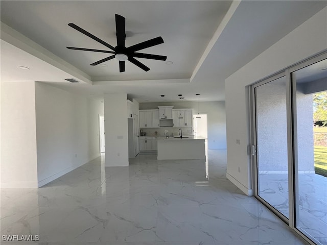 unfurnished living room with ceiling fan, a tray ceiling, and sink