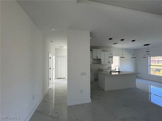 kitchen with sink, a center island with sink, white cabinets, and decorative light fixtures