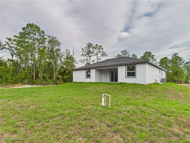 621 Allison St E, Lehigh Acres, FL 33974 - rear view of house with stucco siding, cooling unit, and a lawn
