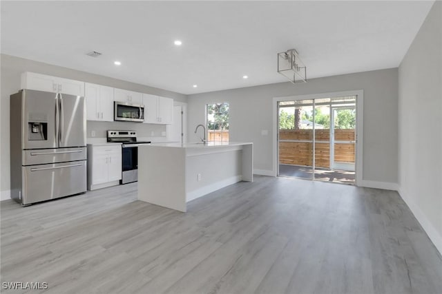 kitchen featuring a healthy amount of sunlight, appliances with stainless steel finishes, a kitchen island with sink, and white cabinets