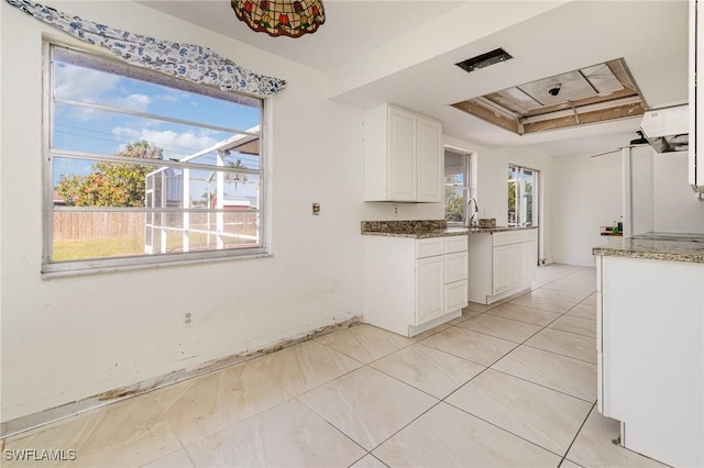 kitchen featuring light tile patterned floors, a sink, white cabinetry, a tray ceiling, and dark stone countertops