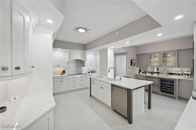 kitchen featuring sink, stainless steel dishwasher, a kitchen breakfast bar, an island with sink, and beverage cooler