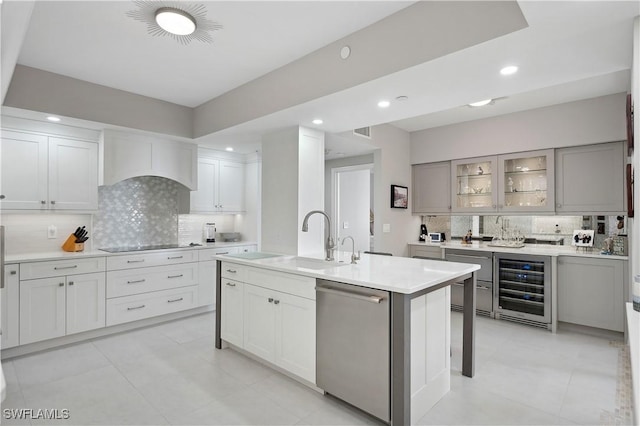 kitchen with sink, black electric stovetop, a center island with sink, stainless steel dishwasher, and beverage cooler