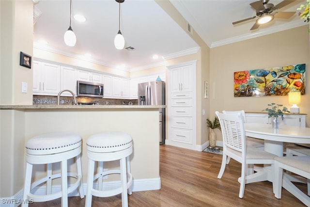 kitchen with appliances with stainless steel finishes, white cabinetry, light hardwood / wood-style floors, kitchen peninsula, and crown molding