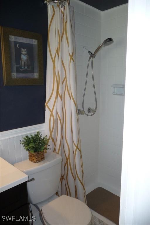 full bathroom with a wainscoted wall, a tile shower, vanity, and toilet