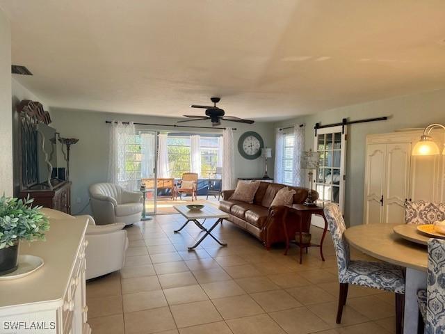 living area with a barn door, light tile patterned flooring, and a ceiling fan