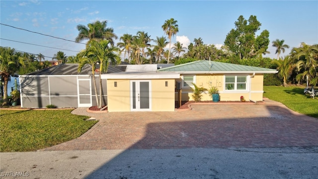 rear view of property with a lanai, french doors, stucco siding, and a lawn