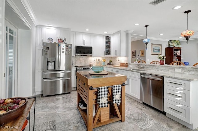 kitchen with a peninsula, ornamental molding, white cabinetry, appliances with stainless steel finishes, and a sink